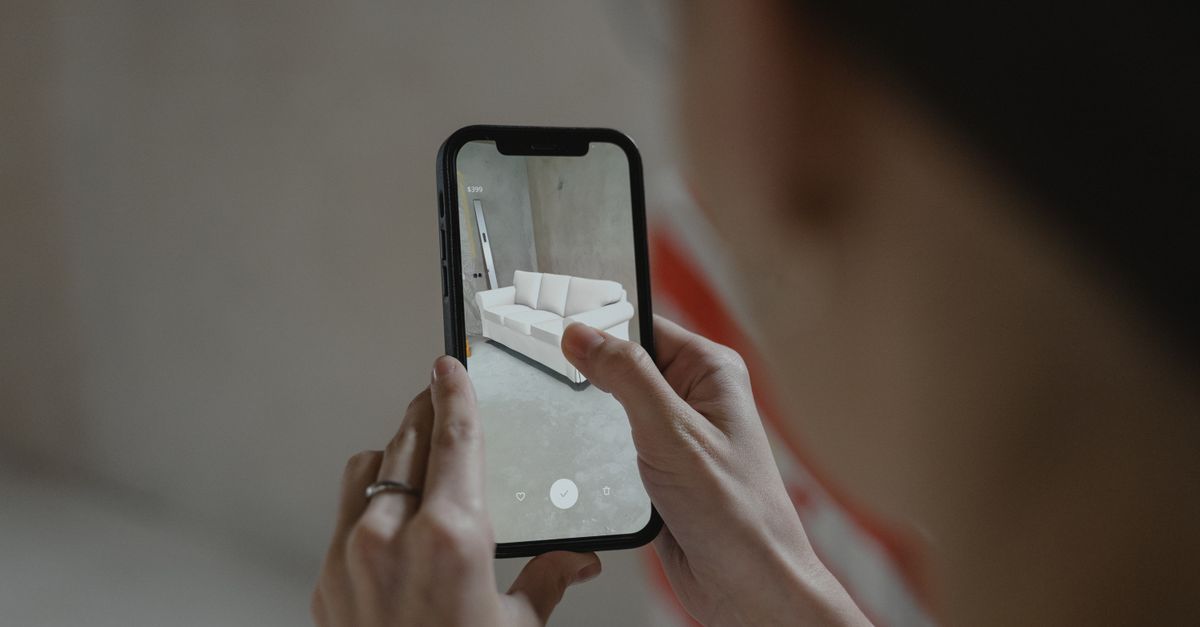 Person using augmented reality on smartphone to visualize a sofa in a room.